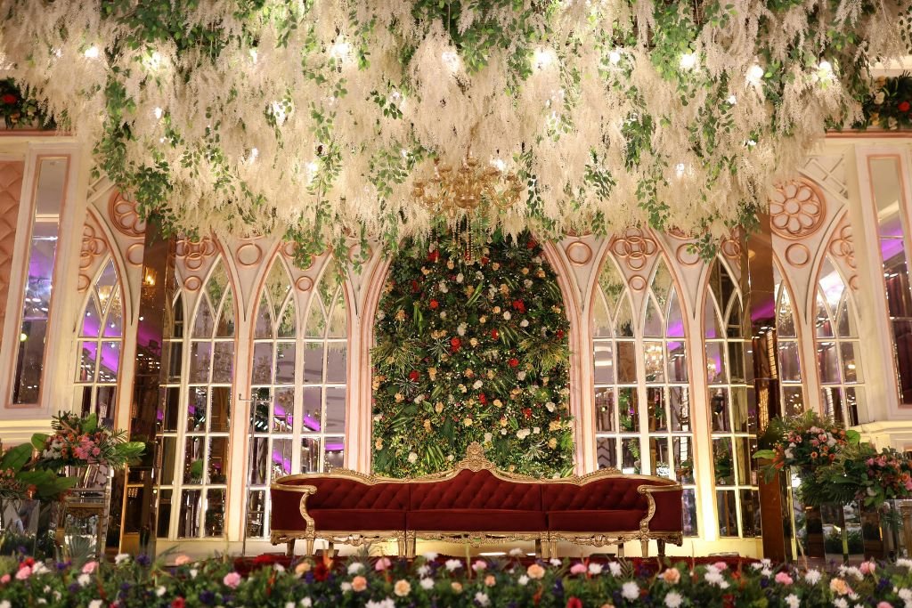 Decorated wedding stage with a floral backdrop and seating, set inside a high arched interior space