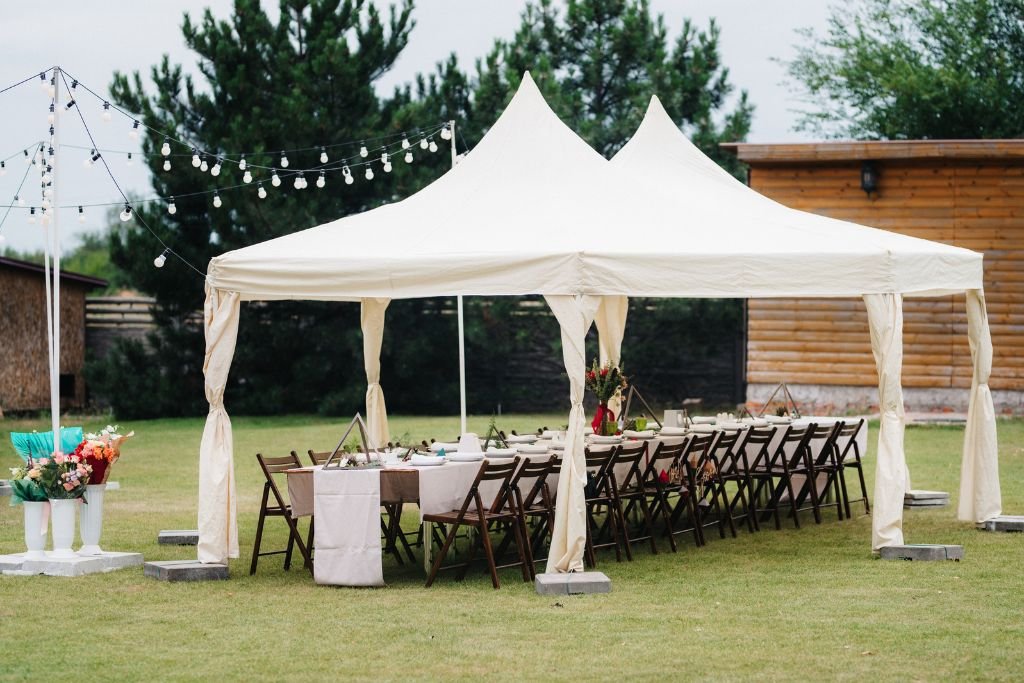 Small white marquee and dressed table on a garden lawn with festoon lighting and trees behind