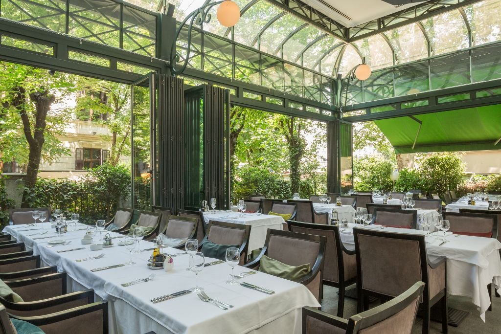 Long dining table set for a wedding inside a glass conservatory surrounded by trees and climbing plants