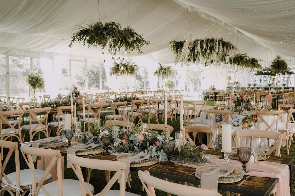 White marquee wedding reception filled with long banquet tables, greenery runners and hanging foliage