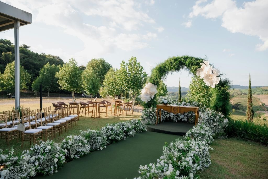 Circular floral wedding arch on an open lawn with white chairs either side and countryside beyond