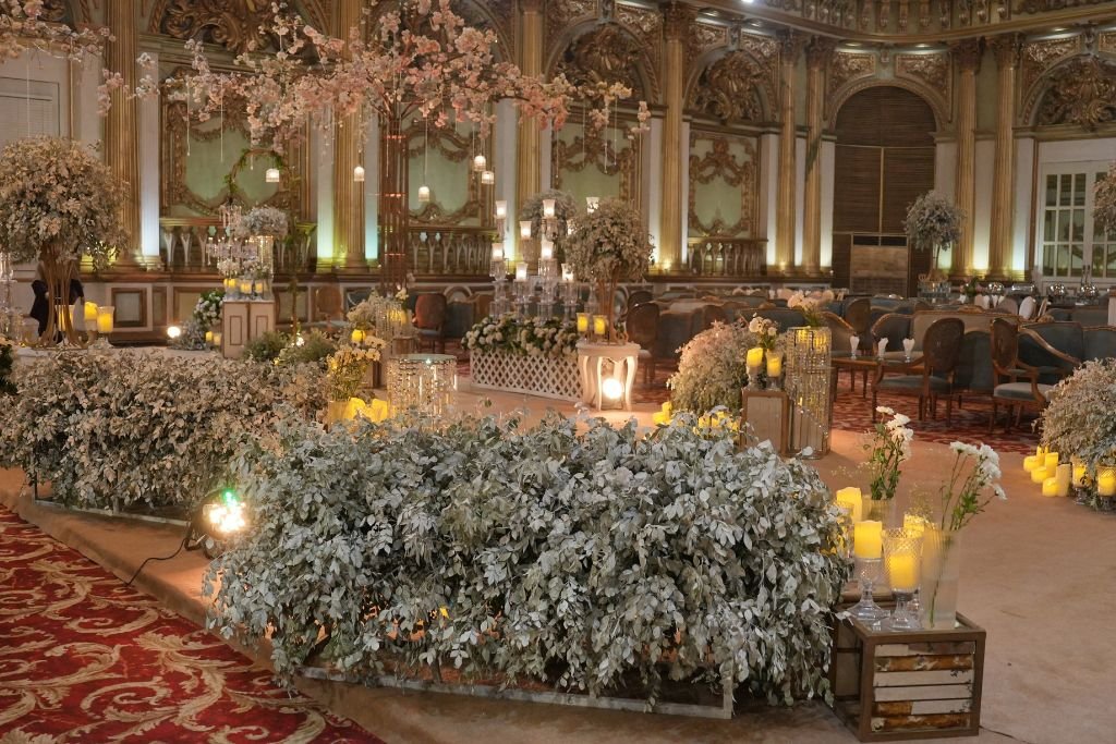 Gilded ballroom set for a wedding reception with floral table runners, candles and patterned carpet
