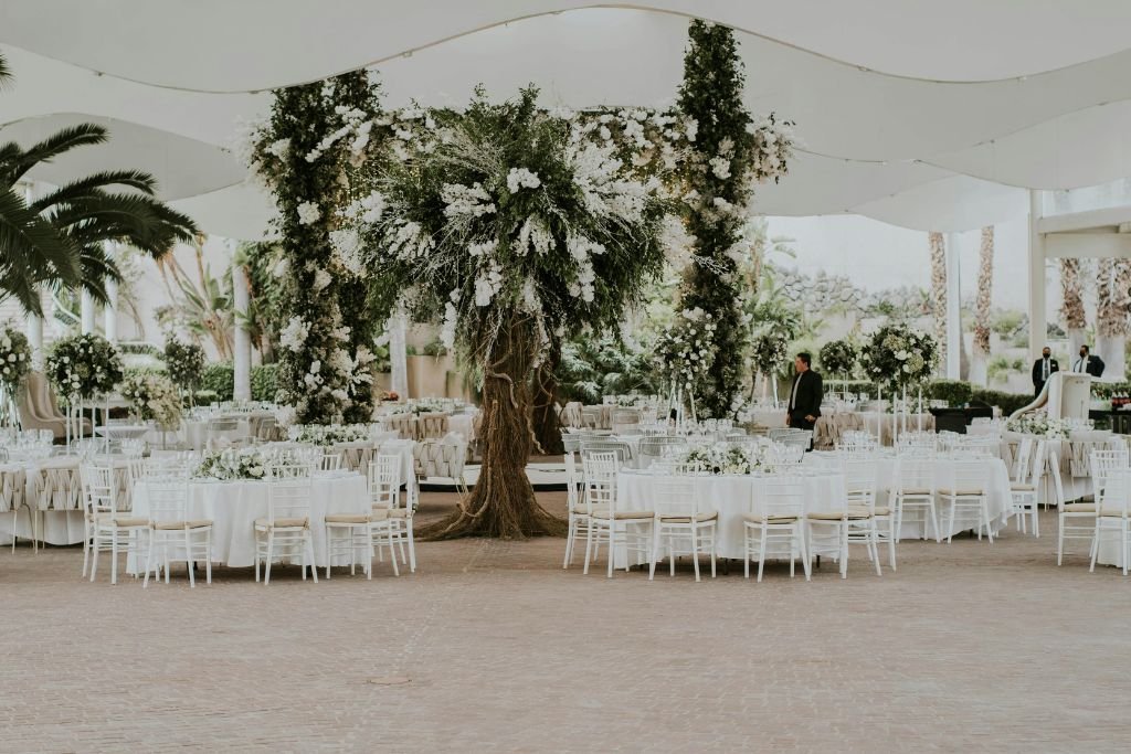 White tented wedding reception with round tables around a large greenery centrepiece